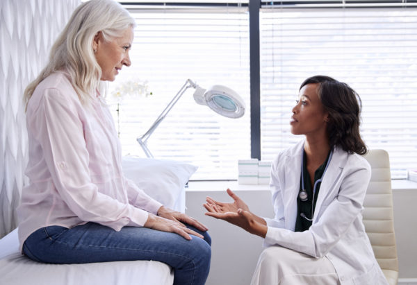 Mature Woman In Consultation for a melanoma treatment With Female Doctor Sitting On Examination Couch In Office