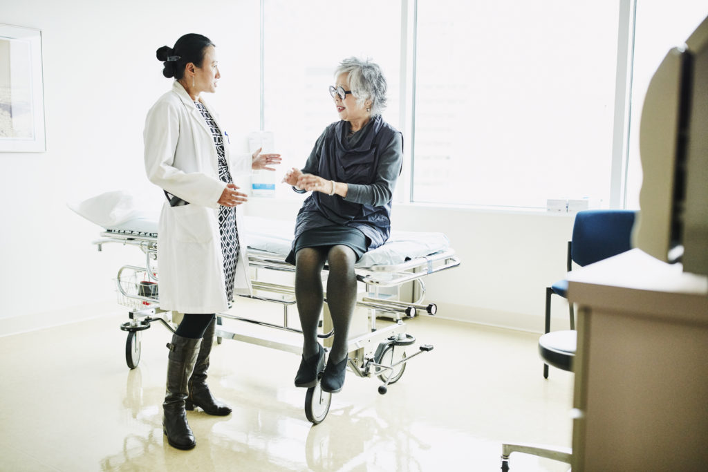 Senior female patient in discussion with doctor during check up in exam room