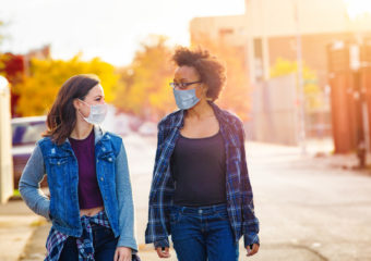 Two female friends walking down a Brooklyn alley wearing face masks