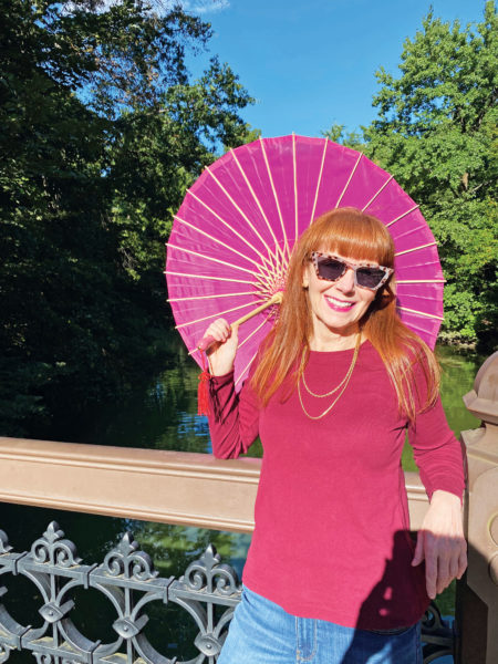 Picture of a woman wearing a pink shirt, a pink parasol and sunglasses. The Skin Cancer Foundation