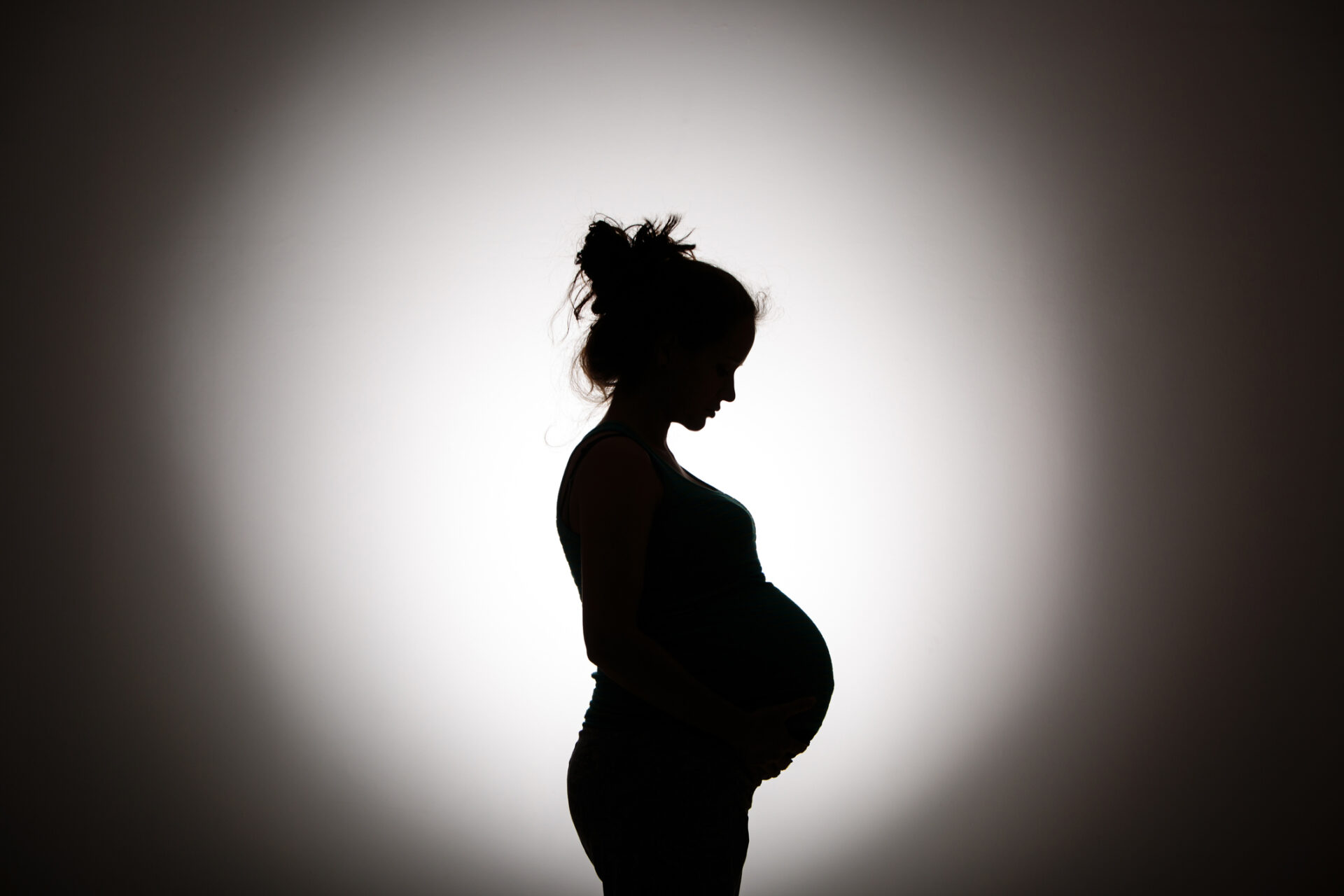 Pregnant woman standing on footbridge holding her pregnant belly in fall  stock photo - OFFSET